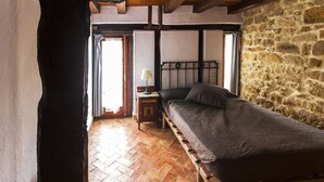 Un dormitorio con cama de madera, mesita de noche, lámpara y pared de piedra.