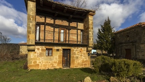 Un edificio de piedra con balcón, entrada protegida por una reja y un pequeño jardín.