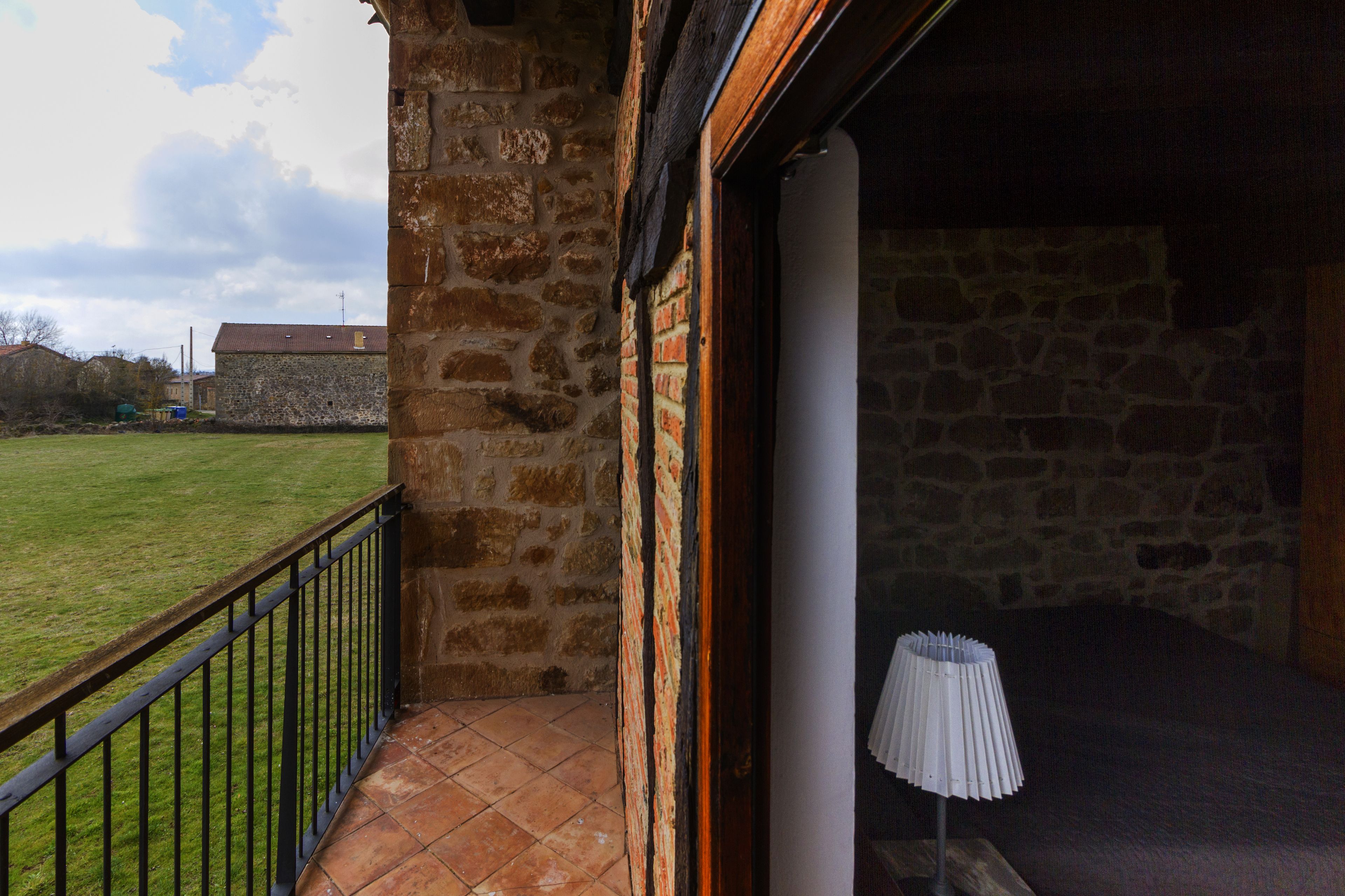 Un edificio de piedra con balcón, una lámpara y un patio cubierto de césped.