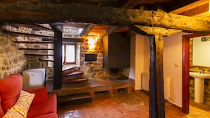 Un interior rústico con pared de piedra, vigas de madera, un sofá rojo, una chimenea y un televisor pequeño.