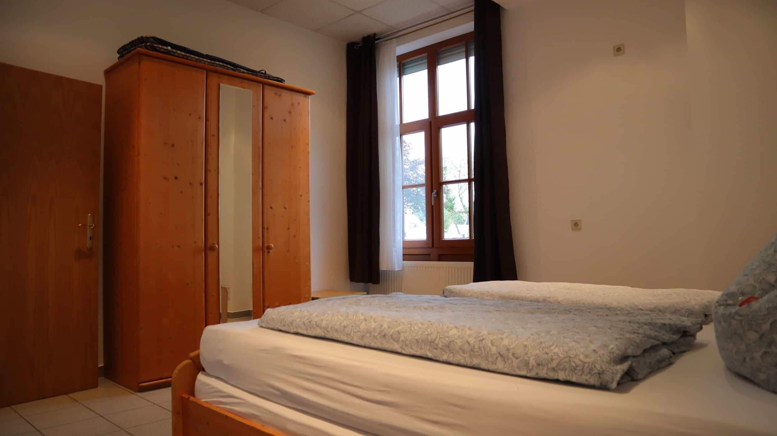 Un dormitorio con un armario de madera, una ventana con cortinas y una cama con colcha estampada.
