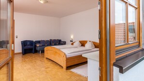 A bedroom with a wooden bed, a sofa, a small table, and a window with a view of buildings. - Toni's Tenne (Eschbach)