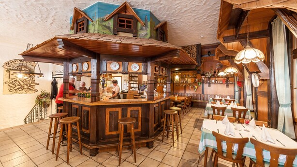 A rustic bar area with wooden decor, a counter, stools, and tables set for dining. - Toni's Tenne (Eschbach)