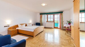 A bedroom with a wooden bed, a nightstand, a chair, a table with a plant, and a view of the outdoors through a window. - Toni's Tenne (Eschbach)