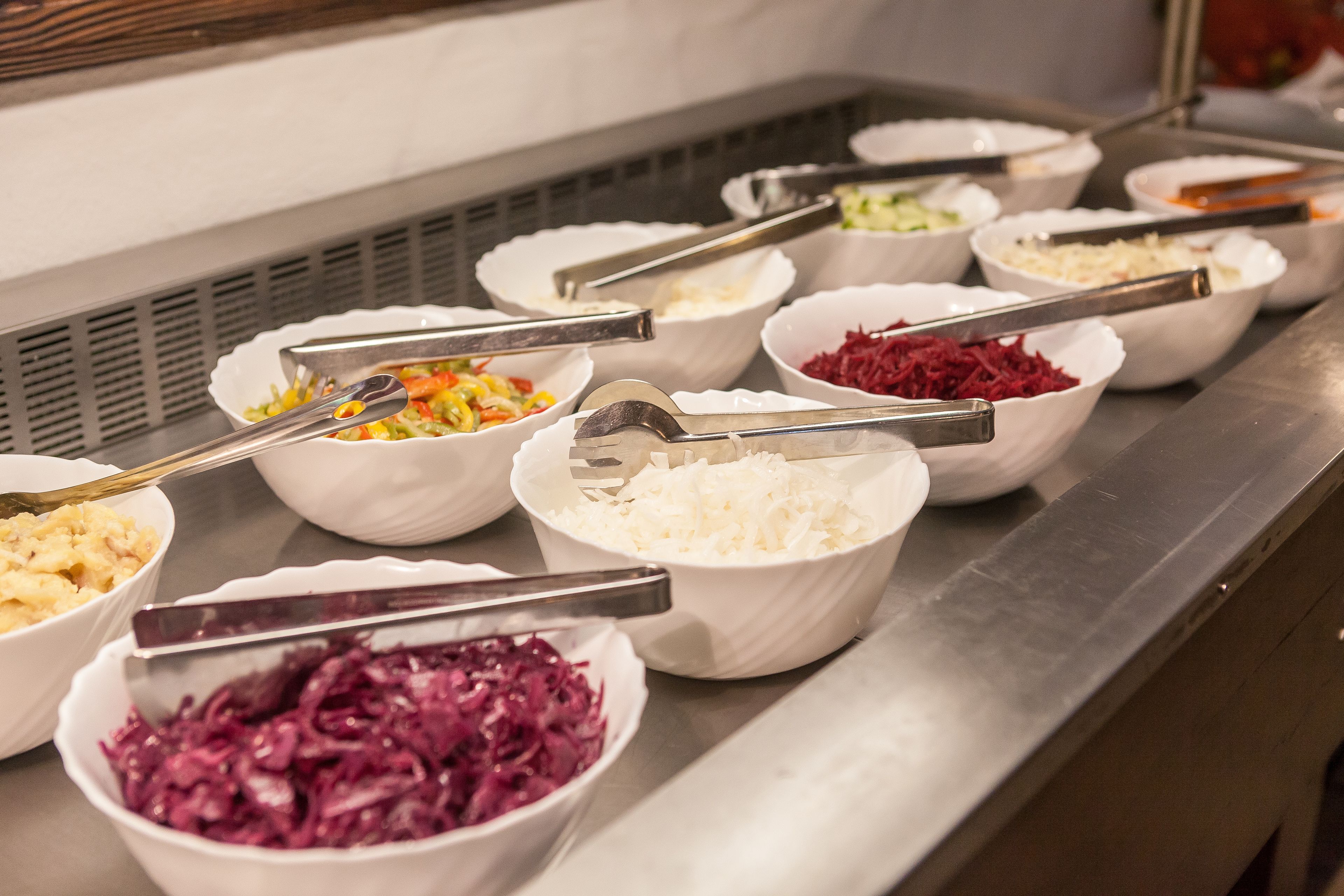 Ein Buffet mit verschiedenen Speisen in Schalen, darunter Krautsalat, geriebener Käse und andere zubereitete Gerichte.