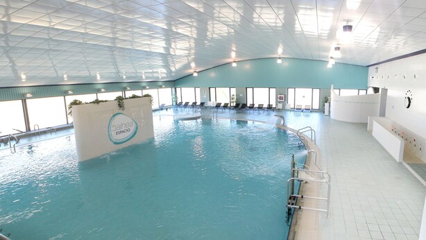 Una piscina interior con suelo de baldosas, una fuente central y una zona de estar con sillas.
