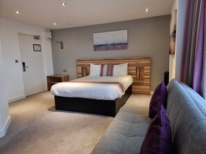 A modern bedroom with a large bed, a grey sofa, and a painting on the wall.