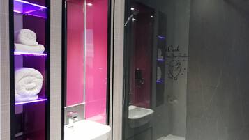 Uma casa de banho moderna com chuveiro em cabine de vidro, toucador com lavatório branco e prateleiras com toalhas dobradas.
