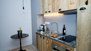 A compact kitchen with wooden cabinets, a sink, a stove, and a small round table with a bottle. - Love Loft (Bordeaux)