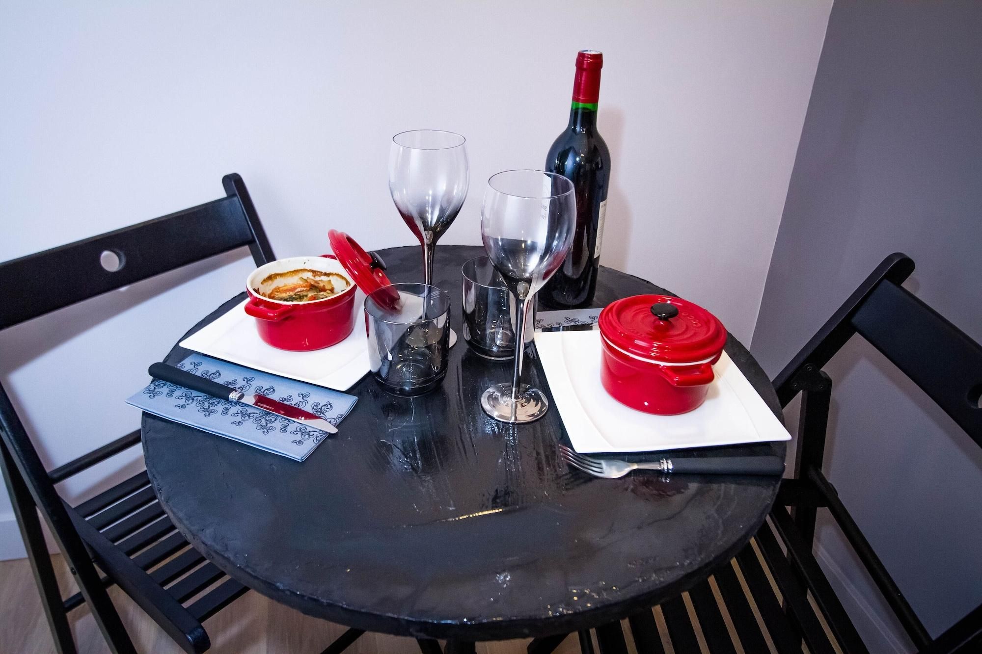 A round dining table with two red pots, two wine glasses, a bottle of wine, and a deck of playing cards.