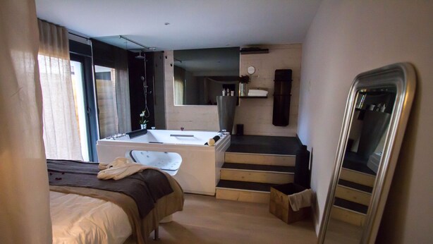 A hotel room with a bed, a bathroom with a bathtub, a mirror, and a staircase. - Love Loft (Bordeaux)