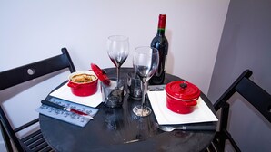 A round table with a bottle of wine, two wine glasses, a red bowl, and a red container on a black chair. - Love Loft (Bordeaux)