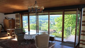 A spacious living room with a large window, a chandelier, and a view of the countryside. - House Luise on Bostalsee, apartment 1: panoramic view and large balcony (Saar)