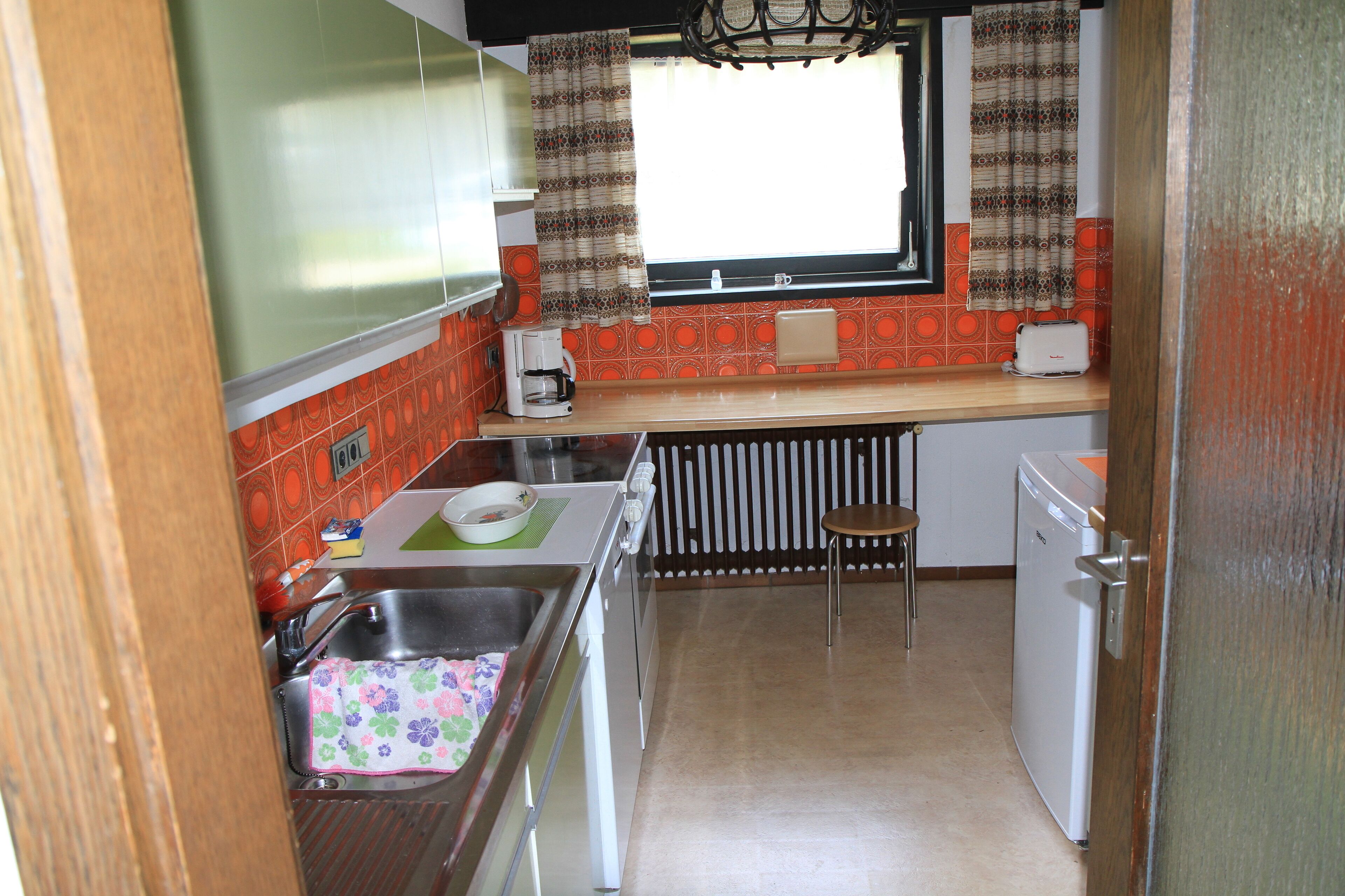 A compact kitchen with a sink, a small countertop, a window with curtains, and a dishwasher.