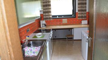 A compact kitchen with a sink, a small countertop, a window with curtains, and a dishwasher.
