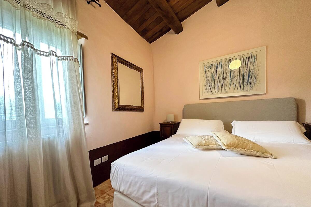 A bedroom with a large bed, a nightstand, a mirror, and a painting on the wall.