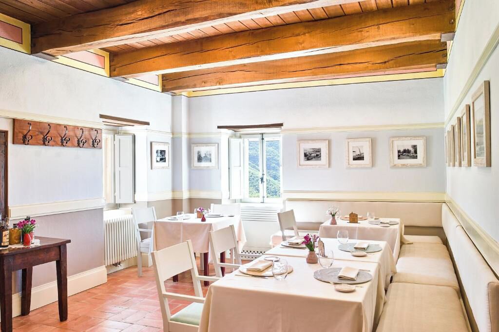 A dining area with tables set for four, wooden beams on the ceiling, and framed pictures on the walls.