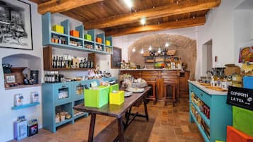 A rustic interior with wooden beams, shelves stocked with various items, and a stone wall.
