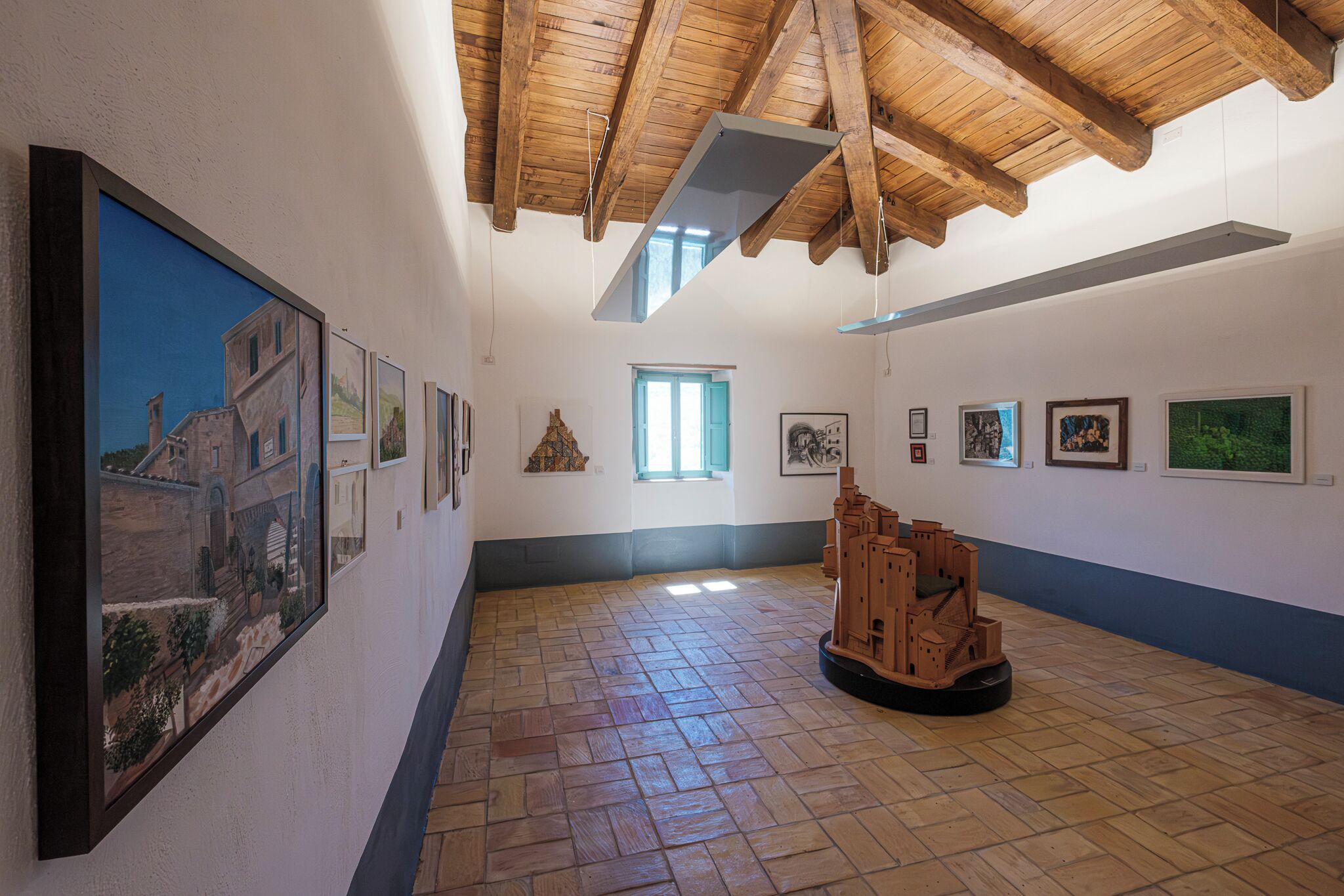 Une galerie d’art dotée d’un plafond en bois, d’un sol en briques et où diverses œuvres d’art sont exposées sur les murs.