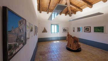 Une galerie d’art dotée d’un plafond en bois, d’un sol en briques et où diverses œuvres d’art sont exposées sur les murs.