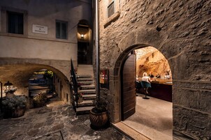 Un edificio de piedra con una entrada arqueada, una escalera y un letrero que dice 'CASTELLO DI POSTIGNANO'.