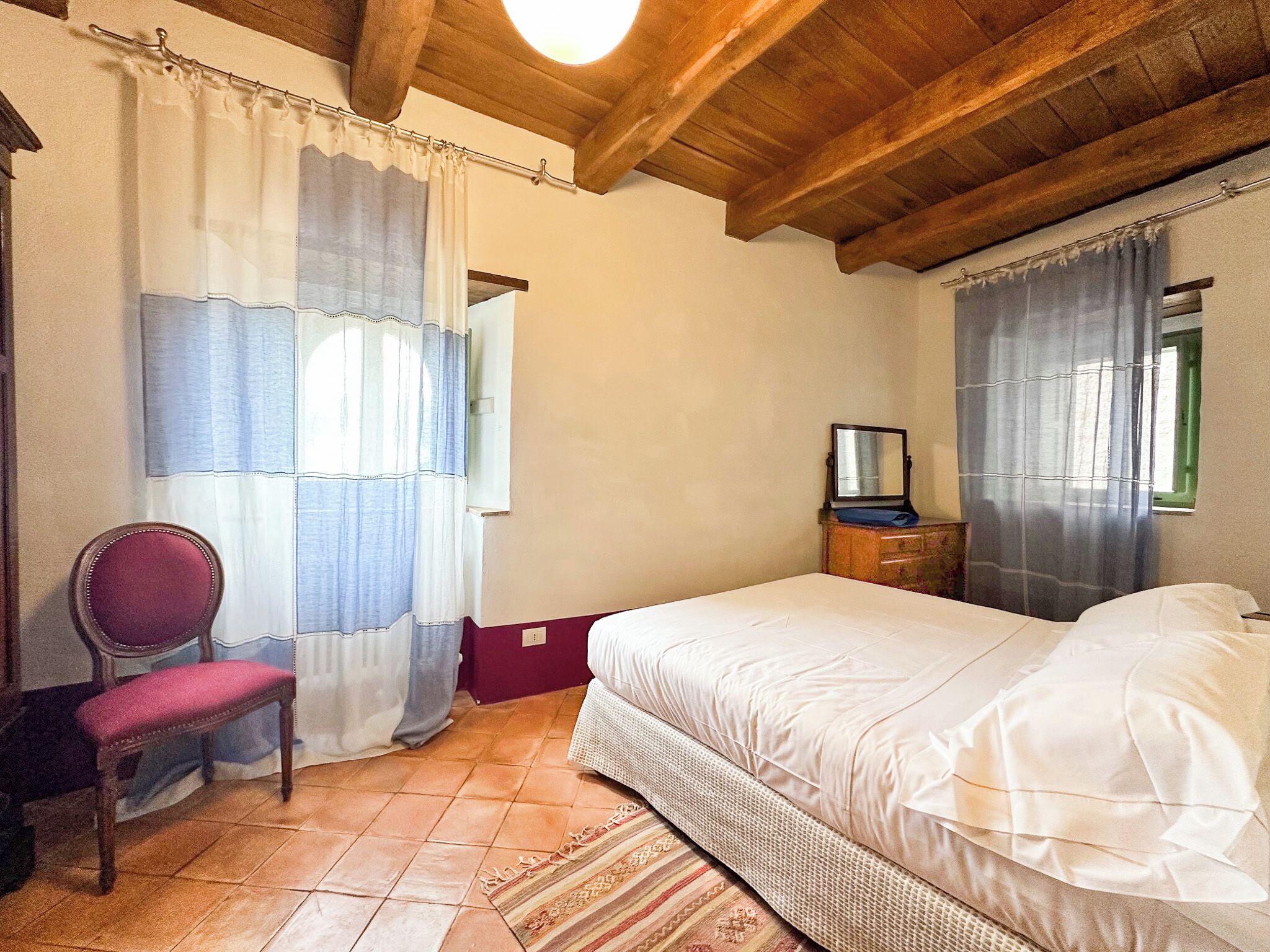 A bedroom with a bed, a chair, a dresser, and a window with curtains.