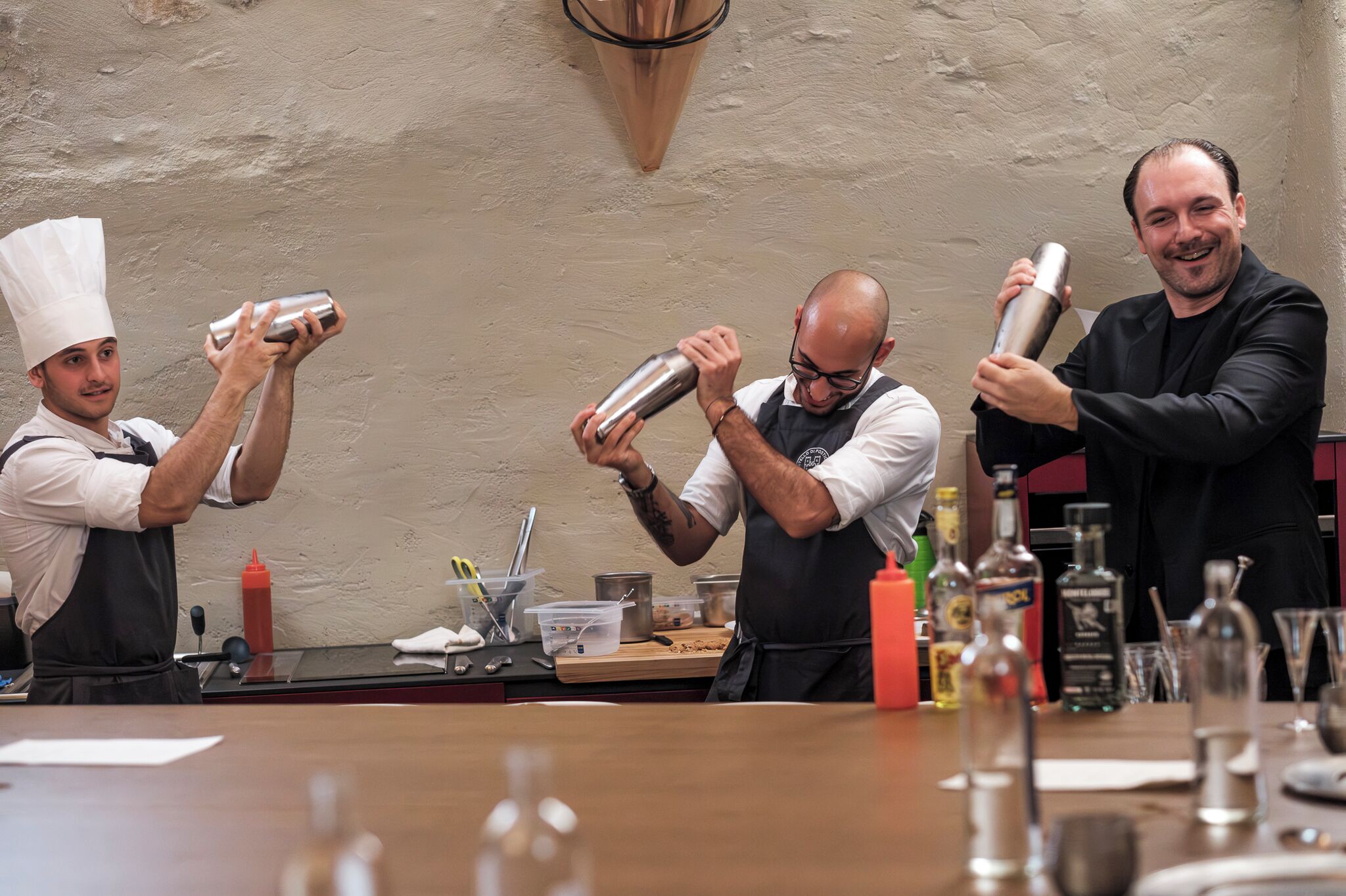 Un bar avec des barmen préparant des boissons, un comptoir où sont exposées différentes bouteilles et un mur à motifs.