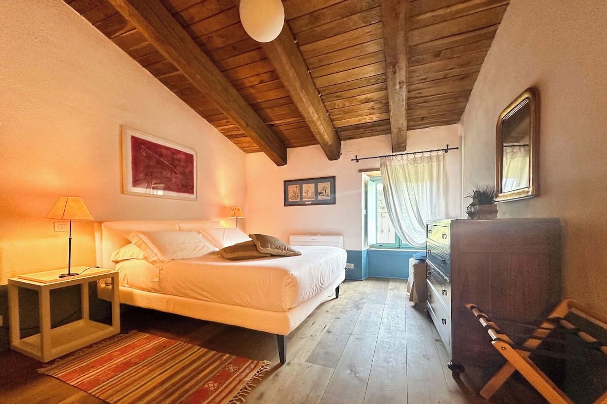 A bedroom with a bed, nightstands, a dresser, a window with curtains, and a wooden ceiling.