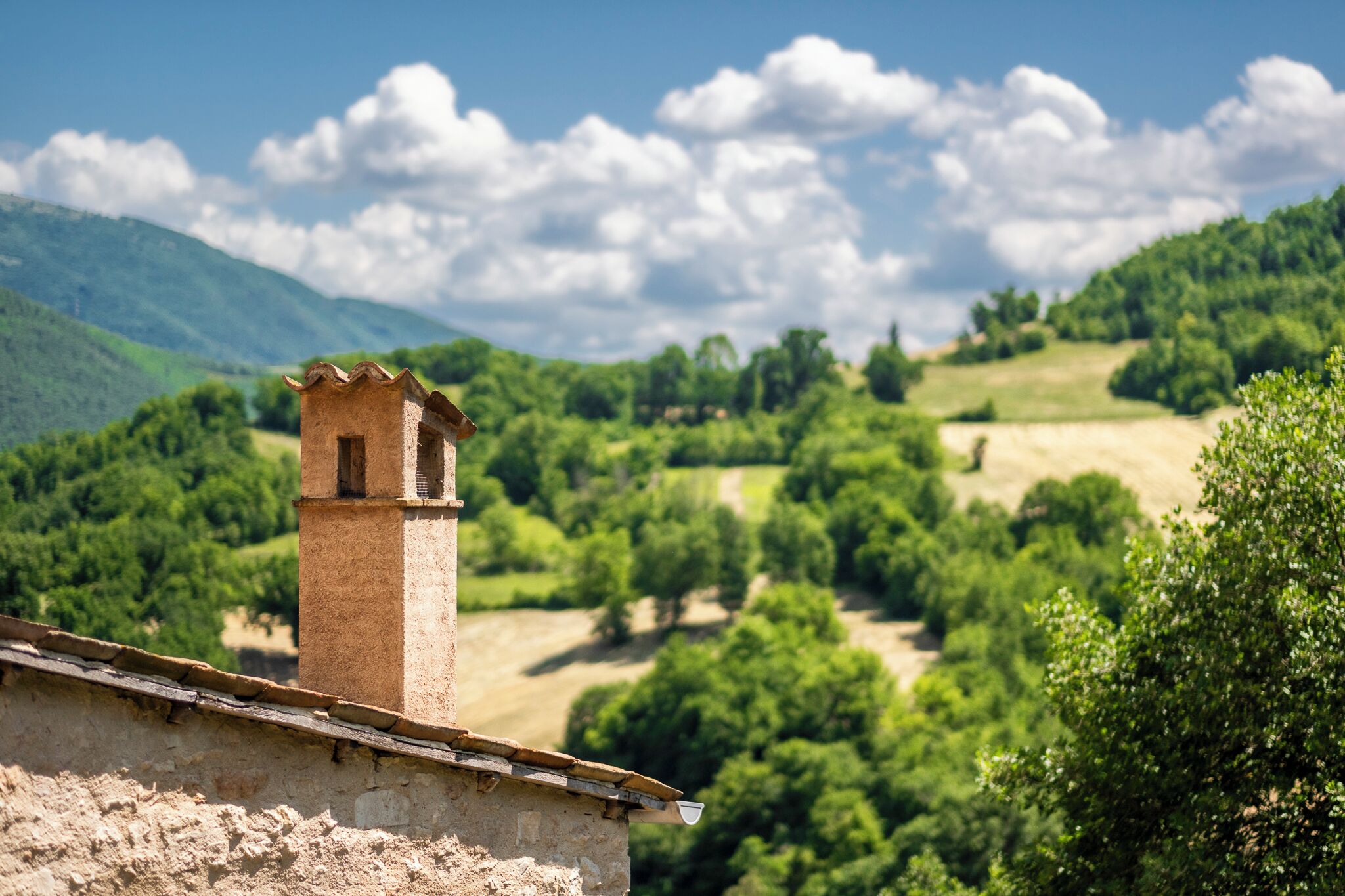 A rustic building with a chimney, surrounded by lush green hills and a clear sky.