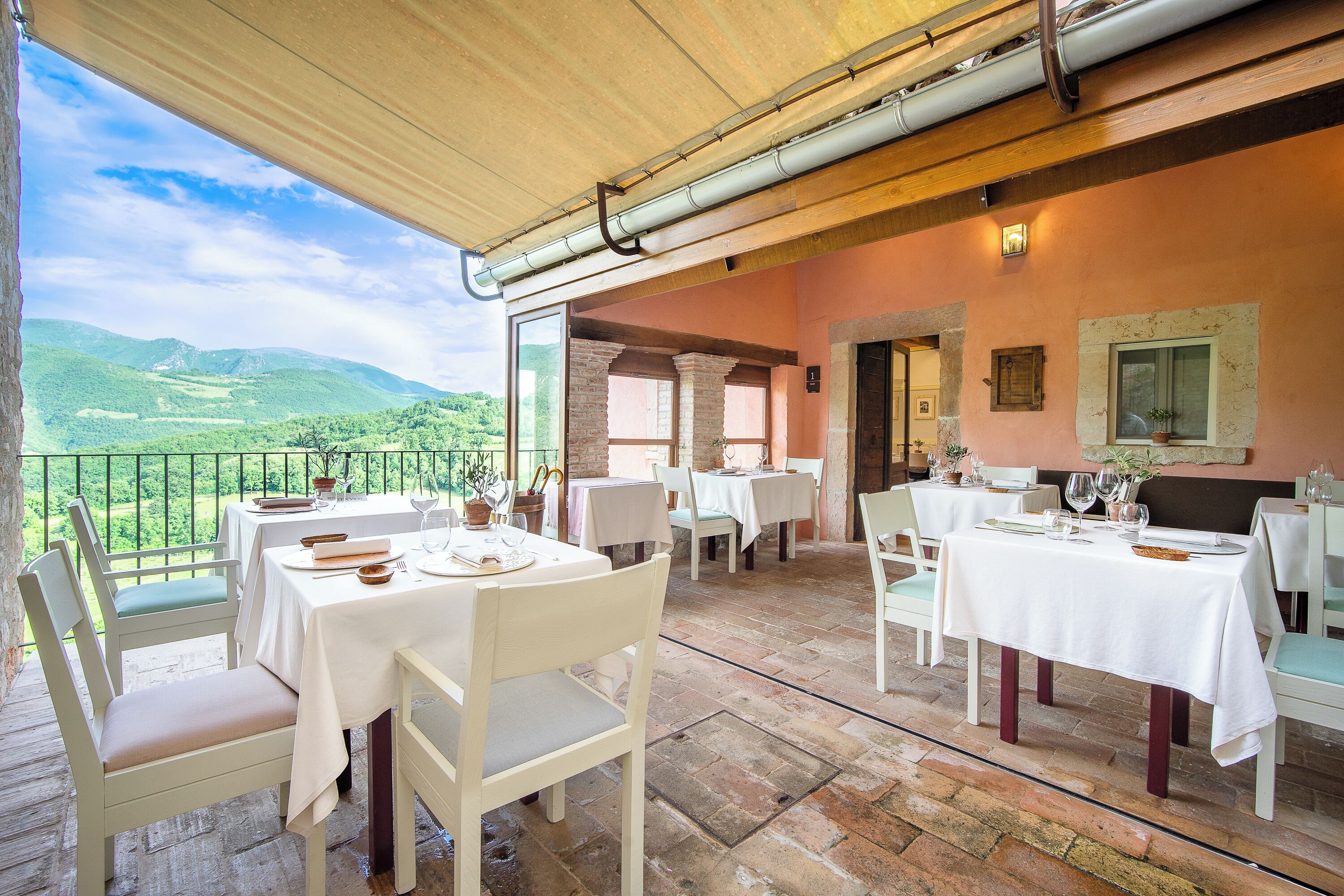 A terrace with tables set for dining, overlooking a mountainous landscape.