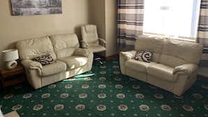 A living room with two beige sofas, a patterned carpet, a chandelier, and a window with striped curtains. - Lyndon Guest House (Inverness)