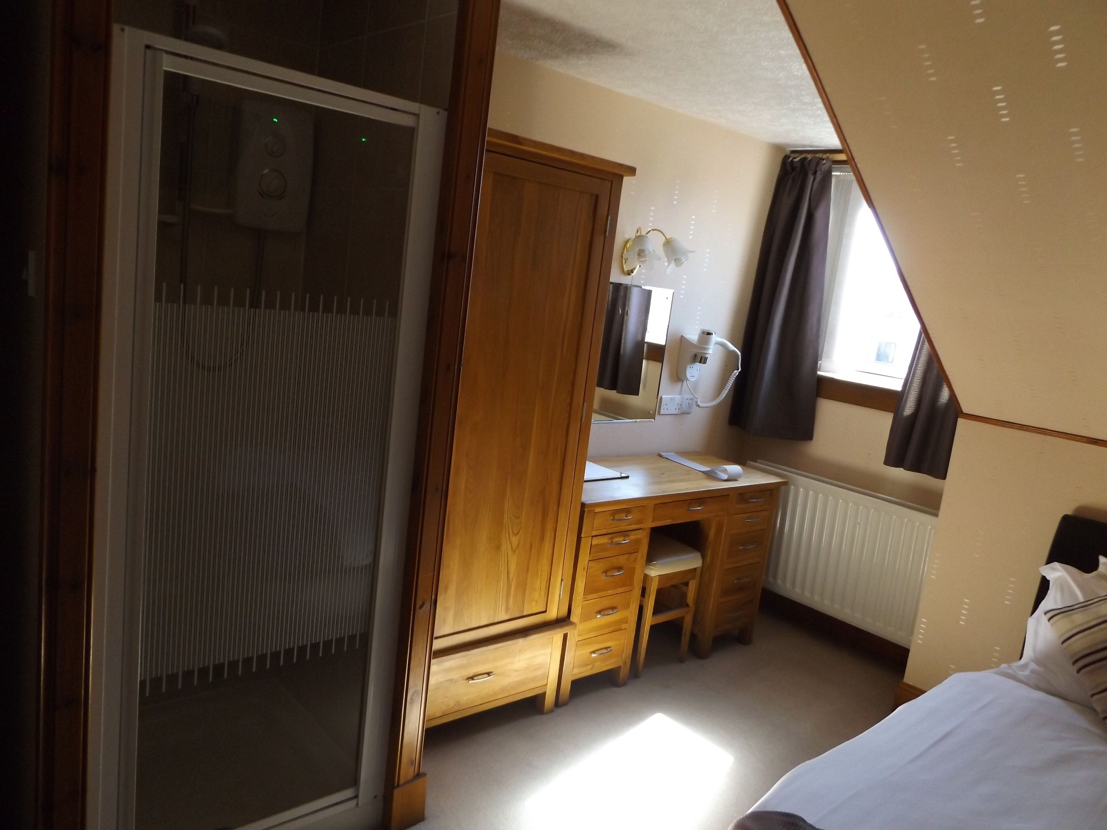 A bedroom with a wooden wardrobe, a desk with a mirror, and a bed.