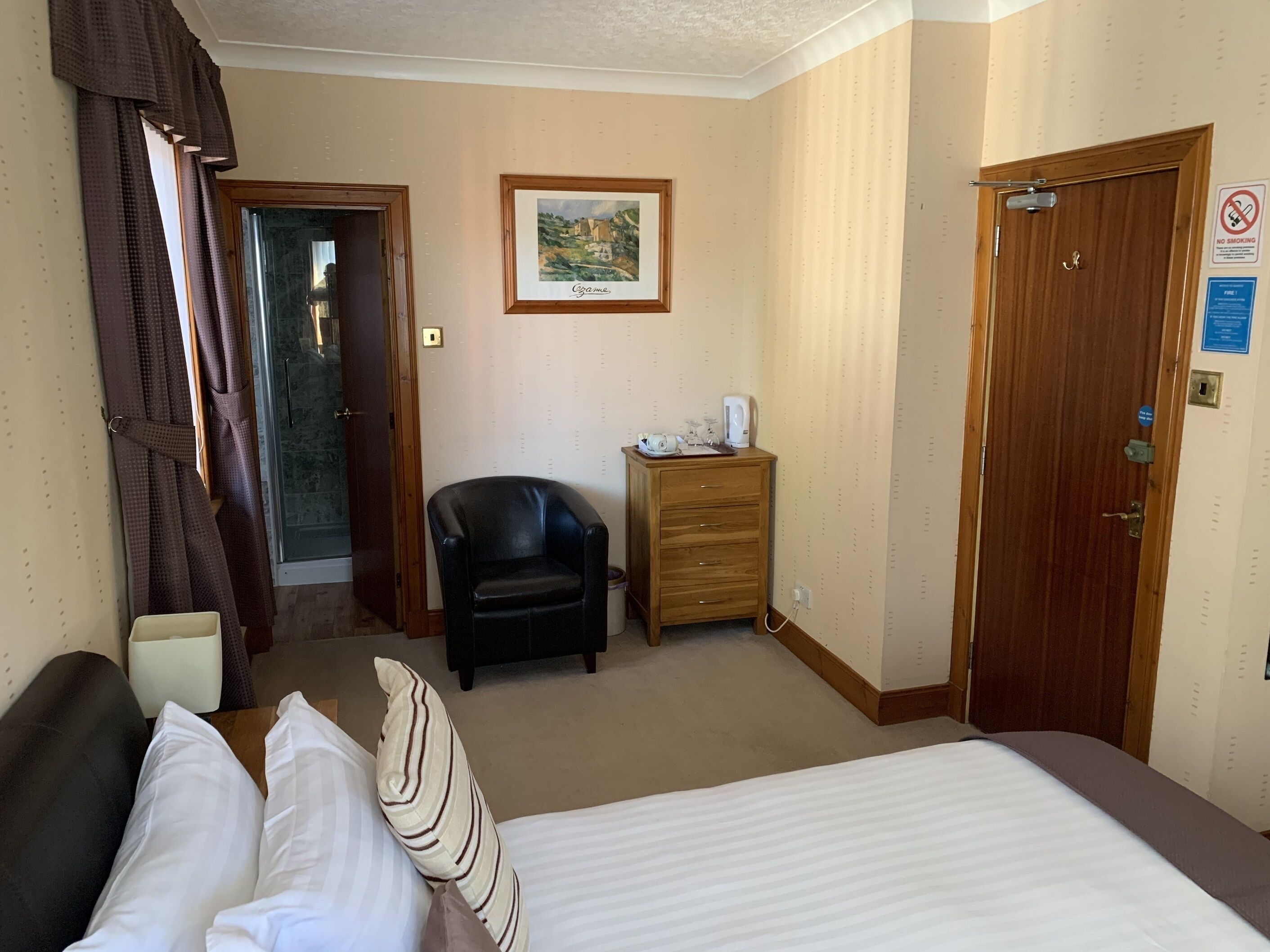 A hotel room with a bed, a chair, a wooden dresser, a door, and a framed picture on the wall.