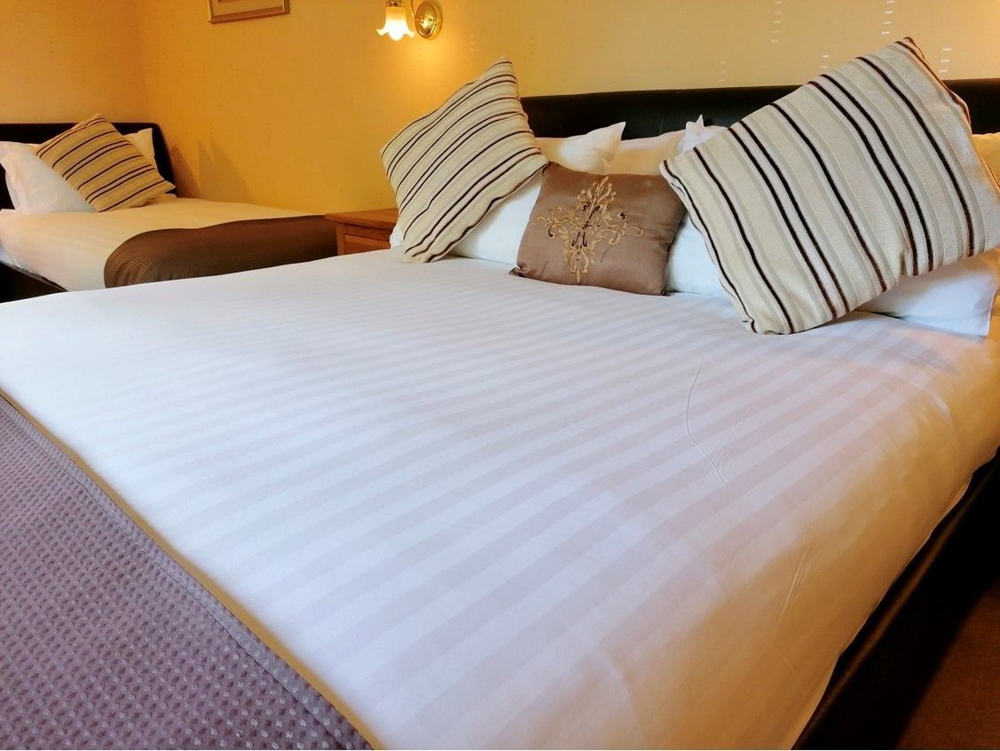 A neatly made bed with striped pillows and a decorative pillow, a bedside table, and a wall-mounted light fixture.