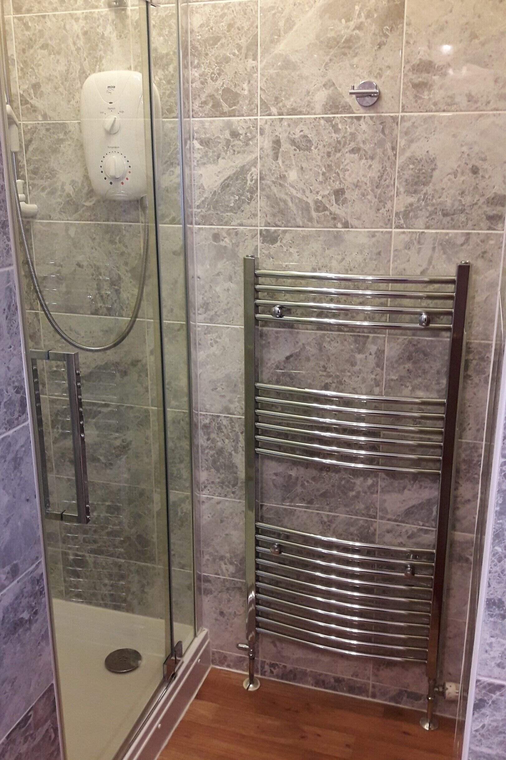 A shower with a glass door, a handheld showerhead, and a wall-mounted control panel.