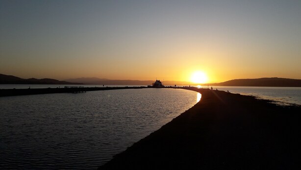 A sunset over a calm body of water with a pier extending into the water. - Lyndon Guest House (Inverness)