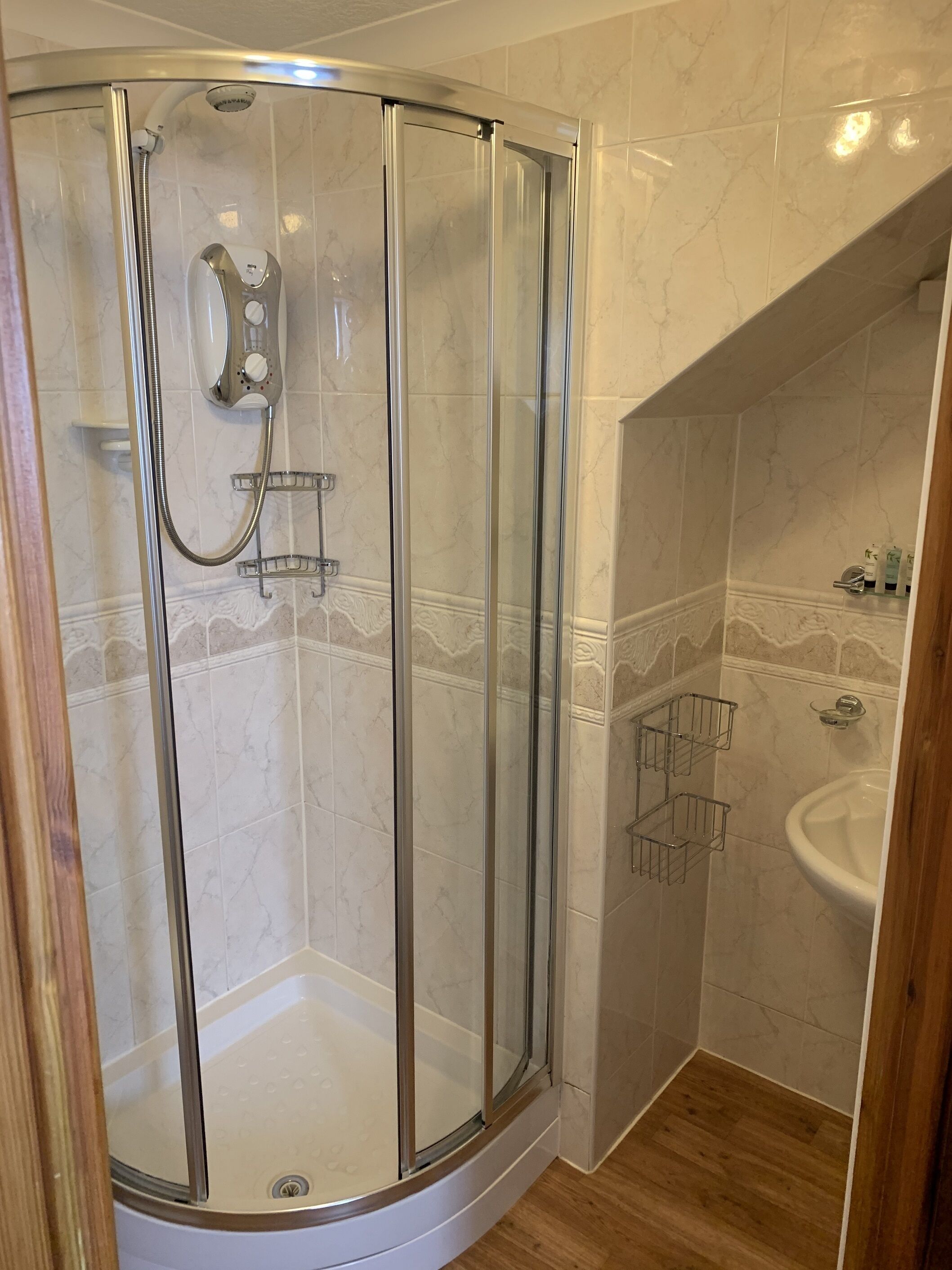 A modern bathroom with a glass-enclosed shower, a pedestal sink, and a wooden floor.