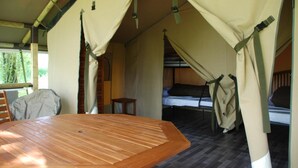 Un hébergement sous tente comprenant une table en bois, des lits superposés et une vue sur la verdure environnante.