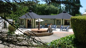 Un espace patio comprenant une table ronde et des chaises, une fontaine en pierre et un coin salon couvert avec des parasols.