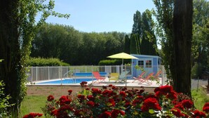 Un espace extérieur clos, doté d’une piscine, de chaises longues et d’un petit bâtiment surmonté d’un parasol jaune.