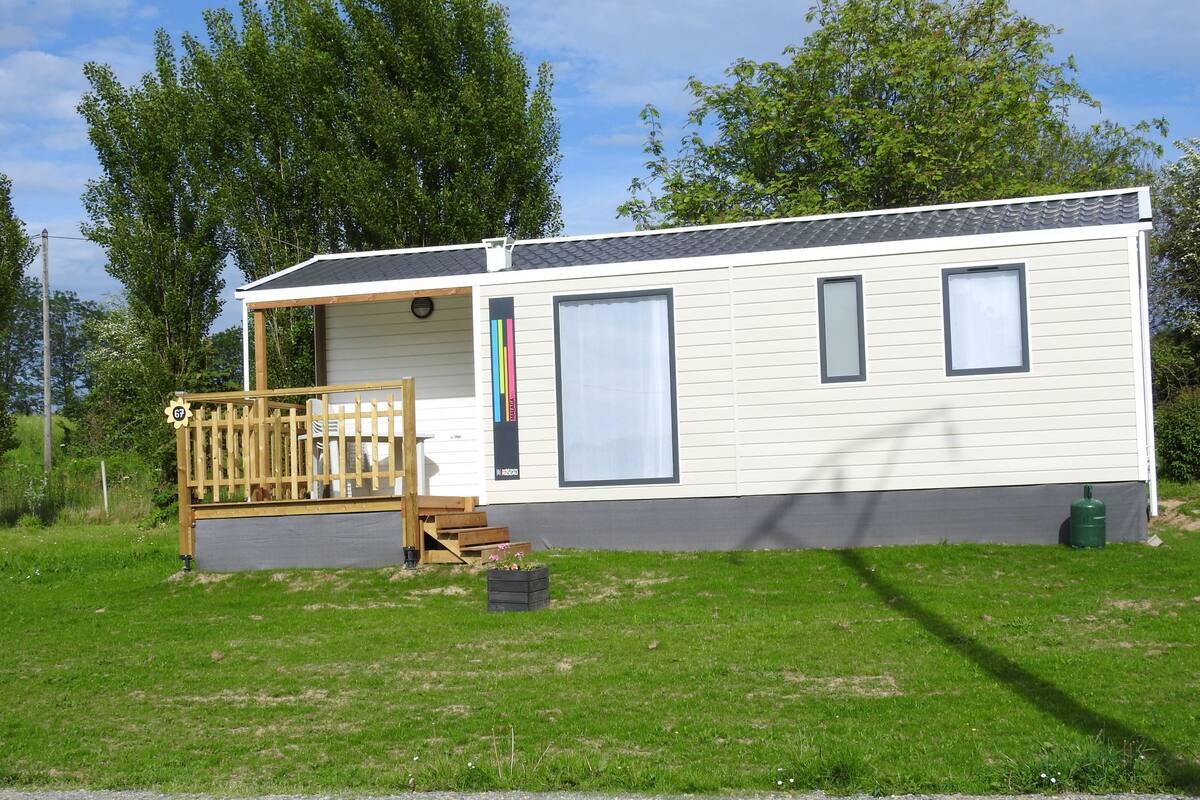 A single-story mobile home with a porch, large windows, and a small deck.