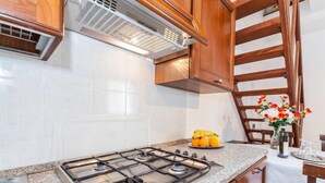 Una cocina con estufa a gas, paredes de azulejos blancos, armarios de madera y un comedor con una mesa dispuesta para dos.