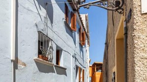 Un estrecho callejón empedrado entre edificios con muros de piedra y contraventanas de madera.