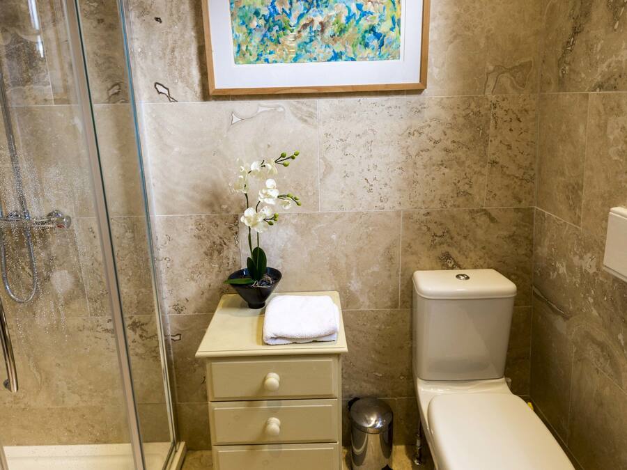 A bathroom with a glass shower enclosure, a toilet, a sink with a towel, and a framed abstract painting on the wall.