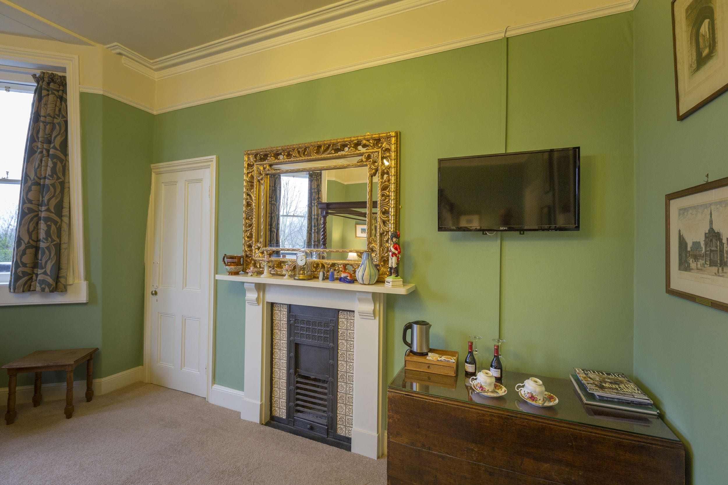 A room with a fireplace, a television mounted on the wall, a door, and a small table.