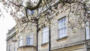 A stone building with a courtyard featuring a round table and chairs, a small garden, and a stone statue. - Grosvenor Villa (Bath)