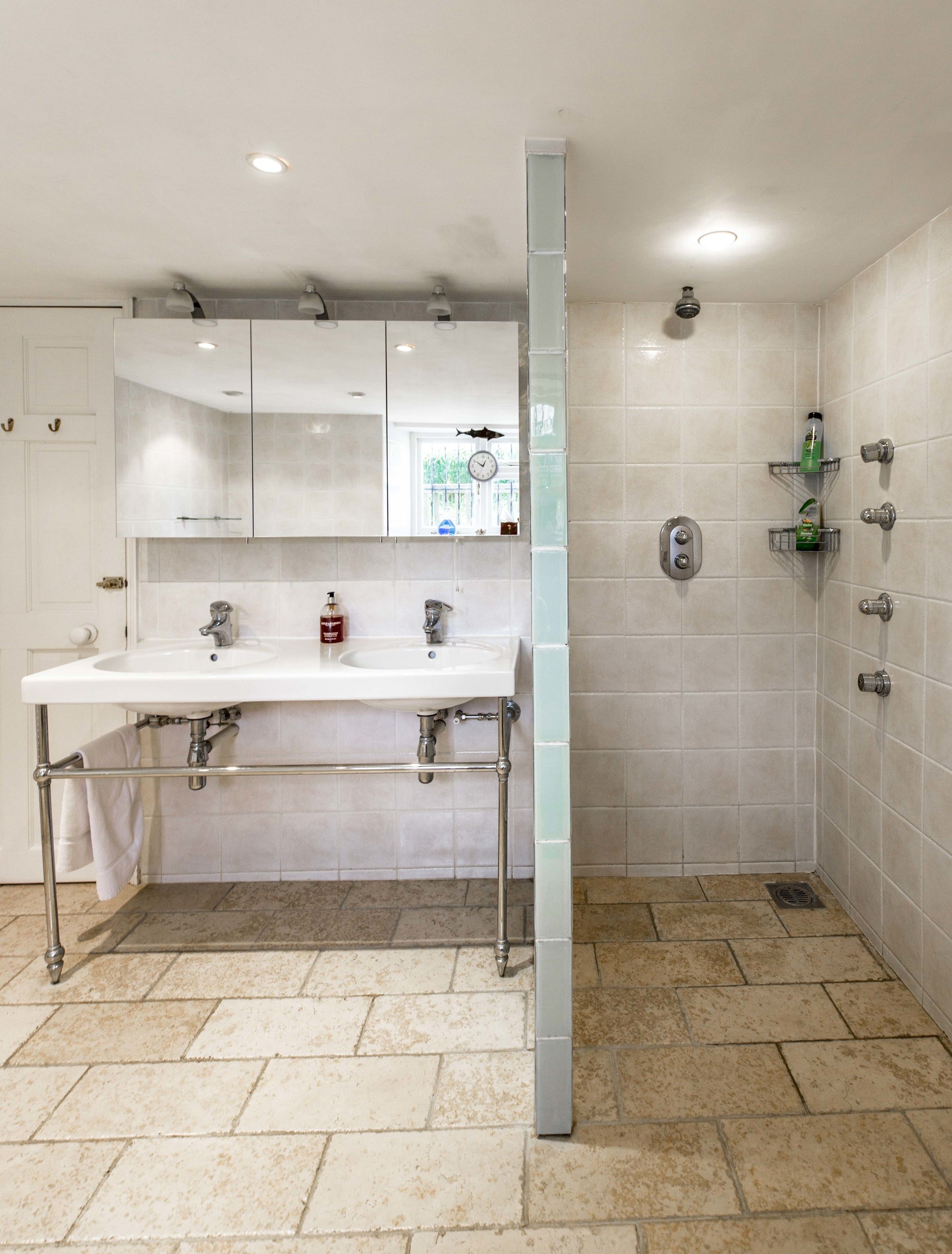A modern bathroom with a double sink, a mirror, a shower, and tiled walls.