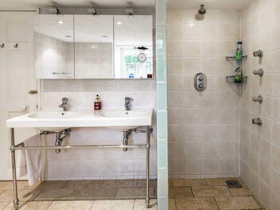 A modern bathroom with a double sink, a mirror, a shower, and tiled walls.