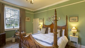 A four-poster bed with a wooden headboard, a bedside table with a lamp, and a window with curtains. - Grosvenor Villa (Bath)