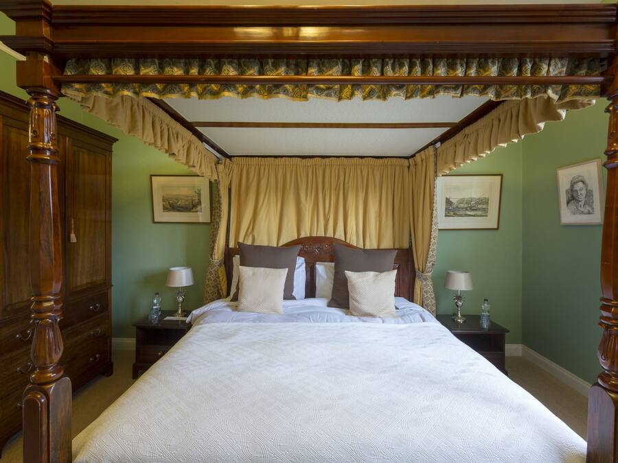 A four-poster bed with a canopy, wooden headboard, and two bedside tables with lamps.